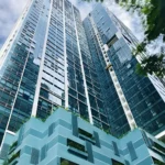 Low-angle view of One Uptown Residence in Bonifacio Global City BGC, Taguig, Manila, featuring a modern glass facade skyscraper with a blue podium and green planter cutouts.