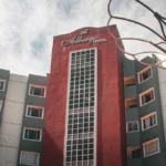 Low-angle view of the multi-story exterior facade of Albergo Hotel in Baguio, featuring a central dark red tower with a grid glass column.
