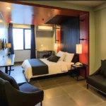 Modern boutique executive room interior at Amelie Hotel Manila, featuring a double bed with dark accents, a grey sofa lounge, and an integrated desk.