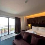 Modern resort bedroom interior at Aozora Seaside Mactan in Cebu, featuring a double bed, dark brown accents, and a sliding glass door leading to a private balcony.
