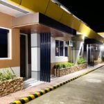 The exterior facade of Arianos Inn in Butuan, Philippines, featuring a row of modern hotel rooms at night, with warm lighting, earth-toned walls, and stone planter boxes along a paved walkway.