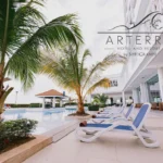 Rows of blue and white lounge chairs beside a large outdoor swimming pool at Arterra Hotel and Resort in Cebu, framed by young palm trees.