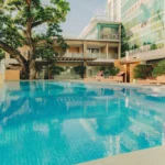 Outdoor swimming pool area with wooden lounge chairs next to a modern condominium building near Ayala Center Cebu