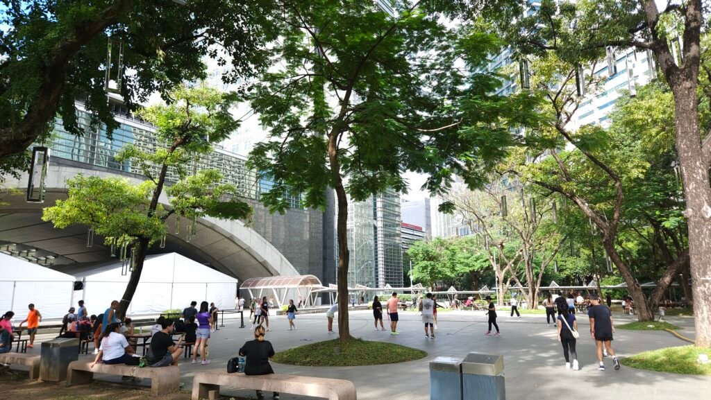Lush green lawns and tall trees of Ayala Triangle Gardens surrounded by modern skyscrapers in the Makati Central Business District, Manila, Philippines.