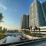 Wide-angle view of the modern, wavy white high-rise residential towers at Azure North in San Fernando, Pampanga, overlooking an outdoor swimming pool complex under a bright sky.