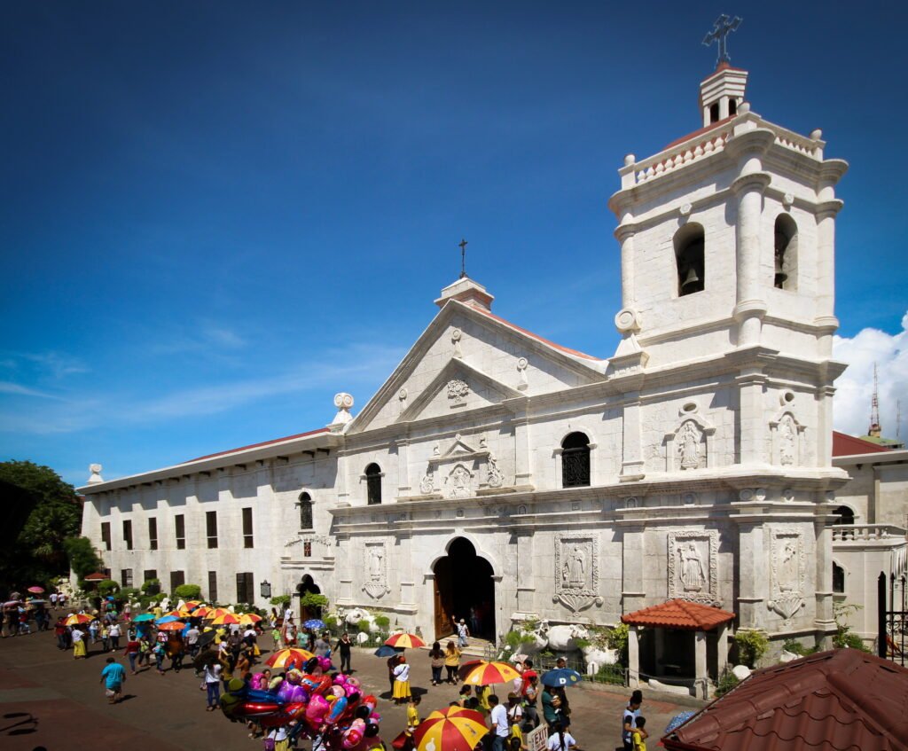 The stone facade and bell tower of the historic Basilica del Santo Niño church in Cebu City, Philippines, under a bright blue sky.