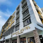 Low-angle view of the modern grey and yellow facade of Bendix Hotel in San Fernando, Pampanga, featuring stone-clad pillars at the entrance under a blue sky.