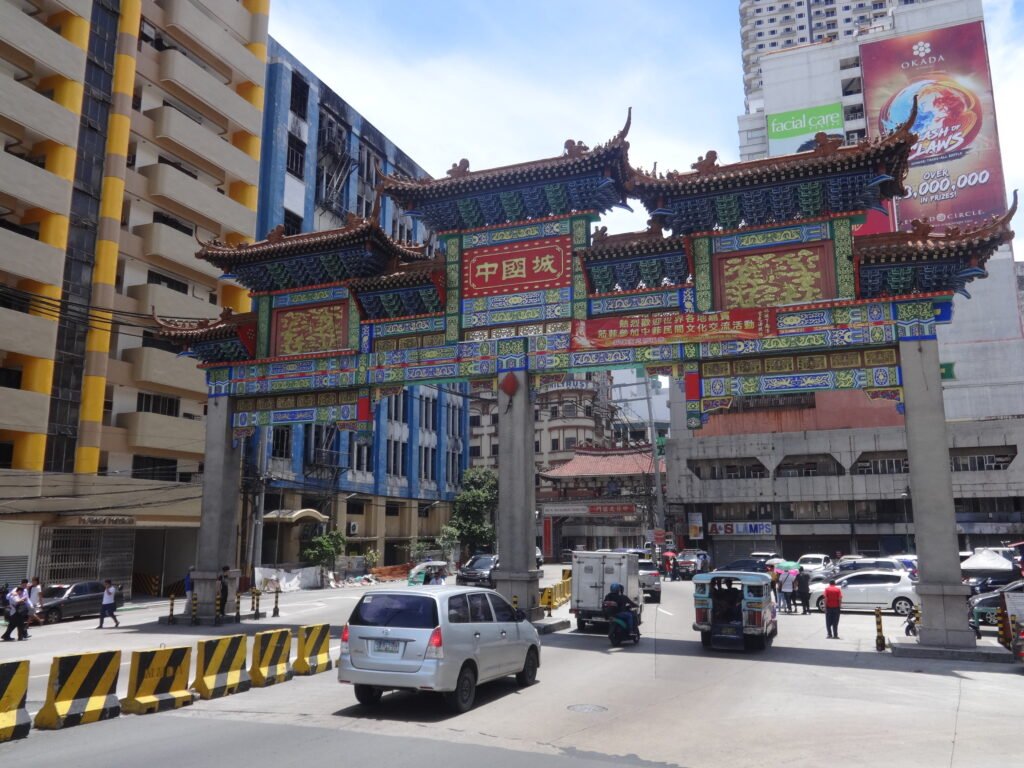 A bustling street in Binondo Chinatown, Manila, featuring colorful Chinese lanterns, historic Filipino-Chinese shopfronts, and local street food vendors.