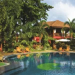 A lush tropical garden surrounding a large swimming pool at Boracay Tropics Resort in Boracay Island, Philippines, featuring traditional Asian-style villas, palm trees, and poolside lounge chairs.