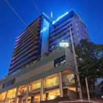 Low-angle exterior view of Cebu Parklane International Hotel at twilight, showcasing its illuminated glass facade, multi-story structure, and ground-level lobby under a deep blue sky.