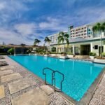 A spacious turquoise outdoor swimming pool with a stone deck at Centro Spatial Bolton Extension in Davao City, featuring residential buildings and palm trees under a bright blue sky.