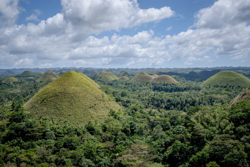 A sweeping panoramic view of the cone-shaped geological formations at the Chocolate Hills Complex in Carmen, Bohol, Philippines under a clear blue sky.