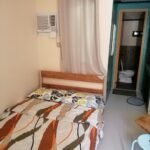 Interior view of a private guest room at CK Homestay Siargao, showing a double bed with patterned sheets, wall air conditioner, and an open bathroom door.