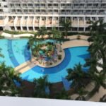High-angle view of the swimming pool complex at Shell Residences in the MOA Complex, Pasay, Manila, featuring palm trees, a central play area, and residential balconies surrounding the pool.