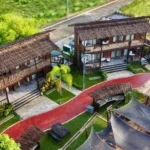 Aerial view of Crusoe Cabins at Costa Azalea in Samal near Davao City, Philippines, featuring two-story wooden beach cabins with thatched roofs and a brick pathway.