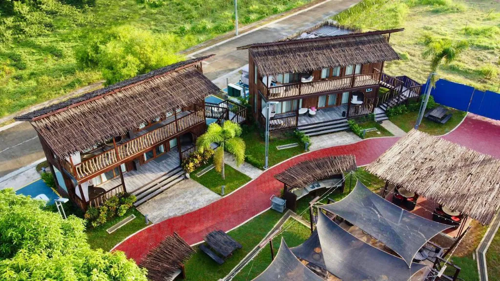 Aerial view of Crusoe Cabins at Costa Azalea in Samal near Davao City, Philippines, featuring two-story wooden beach cabins with thatched roofs and a brick pathway.