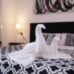 A guest room at D-Gecko Hotel in Cebu, Philippines, featuring a bed decorated with white towel swans, a blue-and-white patterned coverlet, and abstract wall art.