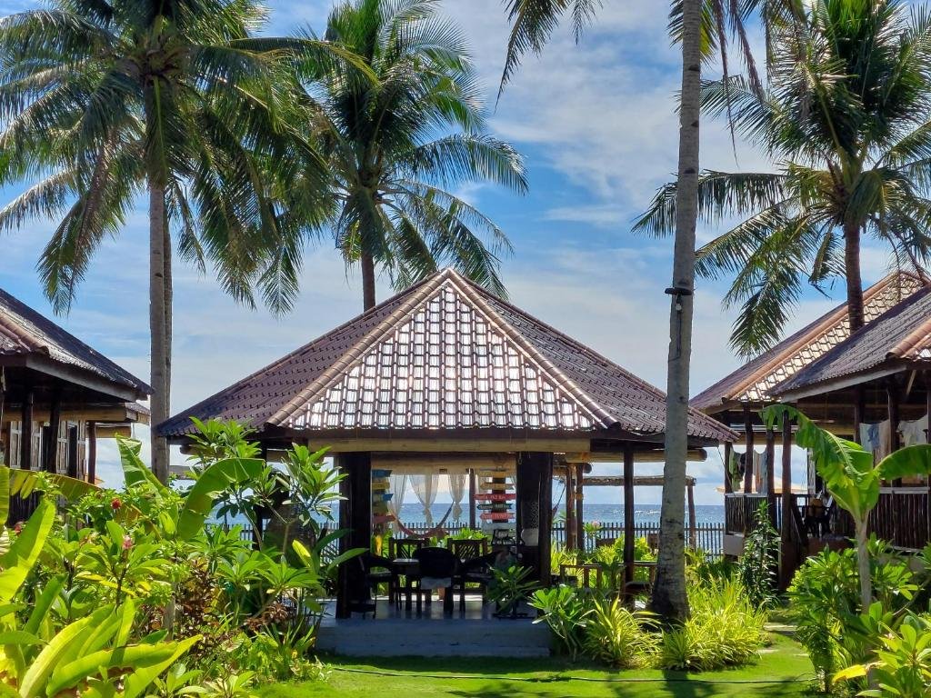 A beautiful open-air beach gazebo with a tiled pyramid roof surrounded by palm trees and tropical plants at DaRosa Del Mar resort in Burgos, Surigao.