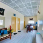 Open-concept living room and dining area of an eight-bed beach house rental in Daanbantayan, Cebu, Philippines, featuring bamboo furniture, tile flooring, and jalousie windows.
