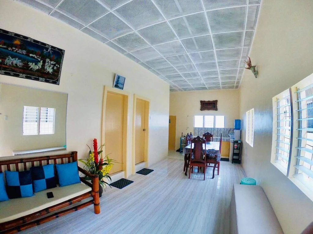Open-concept living room and dining area of an eight-bed beach house rental in Daanbantayan, Cebu, Philippines, featuring bamboo furniture, tile flooring, and jalousie windows.