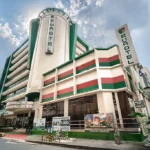 Low-angle exterior view of Eurotel North Edsa Hotel in Manila, showcasing a tall green and beige multi-story building with distinct vertical signage.