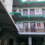Street-level front exterior view of First Baby Byte Guest House in Siquijor, featuring a green gated driveway and a light yellow facade under a bright sky.