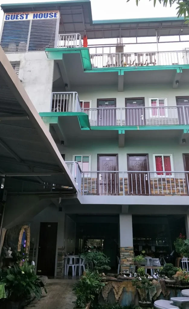 Street-level front exterior view of First Baby Byte Guest House in Siquijor, featuring a green gated driveway and a light yellow facade under a bright sky.