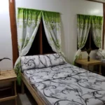 Interior view of a guest room at FN-Lar's Transient in Palawan, Philippines, featuring two beds with black-and-white patterned linens, bamboo side tables, and green-and-white decorative curtains.