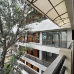 An open-air courtyard view of Franca Arcade near Quezon City Circle, featuring a multi-story white building with glass doors, wooden paneling, and large green trees.