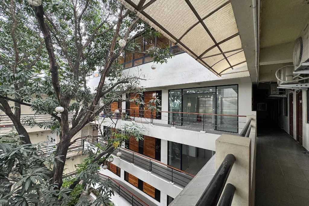 An open-air courtyard view of Franca Arcade near Quezon City Circle, featuring a multi-story white building with glass doors, wooden paneling, and large green trees.