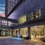 Evening view of the modern glass entrance and drop-off driveway of Hilton Manila at Newport World Resorts, under a twilight sky.