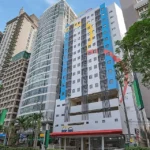 Street-level view of the modern, colorful high-rise building facade of Hop Inn Ortigas Center in Manila, surrounded by tall city skyscrapers.