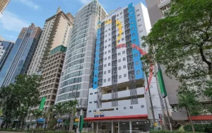 Street-level view of the modern, colorful high-rise building facade of Hop Inn Ortigas Center in Manila, surrounded by tall city skyscrapers.