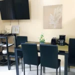 Modern compact dining area at Jazz Staycation in Manila, Philippines, featuring a black glass-top table with dark chairs, a wall-mounted TV, a toaster, and a coffee maker.