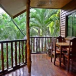 Shaded wooden balcony of La Salangane Caalan Beach Villa in Palawan, featuring a rustic dining set overlooking dense green tropical palm trees.