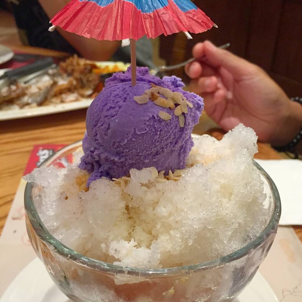 A colorful glass of traditional Filipino halo-halo dessert topped with ube ice cream, leche flan, and shaved ice, served at a popular beachside spot in La Union.