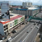 High-angle aerial drone view of Leope Hotel Cagayan in Cagayan de Oro, showing its cream building with a green-trimmed facade next to a multi-lane highway and a Gaisano mall.