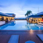 Evening view of the rooftop infinity swimming pool at L'Fisher Chalet in Bacolod, Negros Occidental, Philippines, featuring an illuminated pool, a poolside gazebo bar, dining patios, and lounge chairs at twilight.