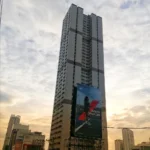 Low-angle exterior view of a towering gray and white high-rise residential condominium building at sunset under a cloudy sky.