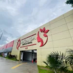 Low-angle view of the exterior entrance of Maganda Drive-In Hotel in San Fernando, Pampanga, showing a tan facade with a red logo under an overcast sky.