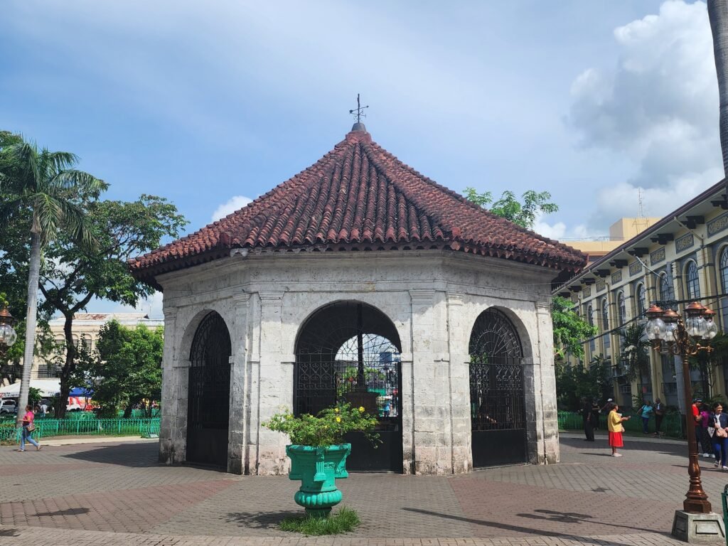 The historic Magellan's Cross enclosed in a wooden kiosk with vibrant ceiling paintings depicting the arrival of Spanish colonizers in Cebu, Philippines.