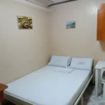 Interior view of a compact budget double room at Magic Square Inn in Naga City, showing a white metal bed, a small white plastic desk, and a wall cabinet.