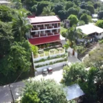 Aerial view of Mansion Buenavista boutique hotel in El Nido, Palawan, Philippines, showcasing its multi-tiered balconies, red metal roof, and lush tropical jungle surroundings.