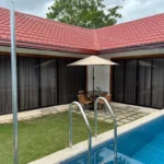 An outdoor private swimming pool and courtyard patio with a dining table under a beige umbrella at Manta Dream Villas in Bohol.