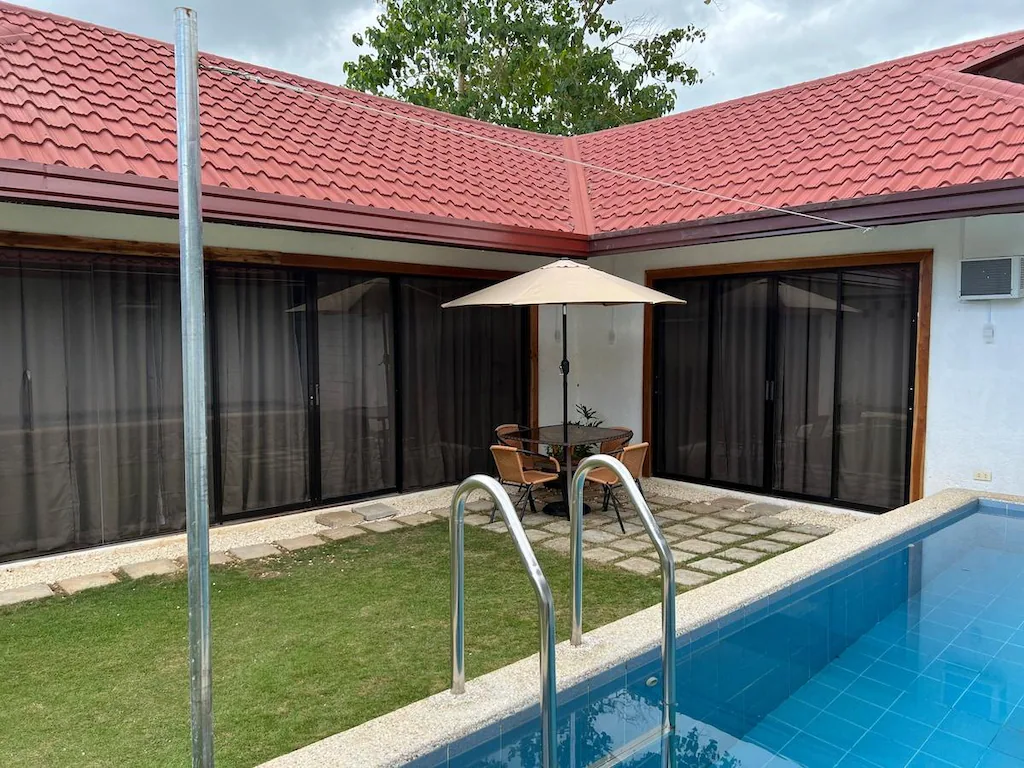 An outdoor private swimming pool and courtyard patio with a dining table under a beige umbrella at Manta Dream Villas in Bohol.
