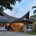 Low-angle outdoor view of the main lobby entrance at Matabungkay Beach Hotel in Batangas, featuring a sweeping shingled roof with pointed peaks and a lit porte-cochere.
