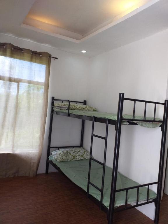 A modern bedroom inside Mia and Miguel's House in General Trias, Philippines, featuring a black metal bunk bed with green bedding, wood-look flooring, and a large curtained window.