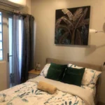Interior view of a modern, bright condominium living room in Quezon City, featuring a gray sectional sofa, geometric accent wall, and a view of a dining table.