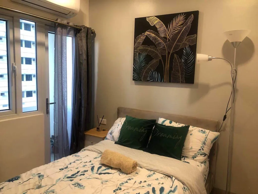 Interior view of a modern, bright condominium living room in Quezon City, featuring a gray sectional sofa, geometric accent wall, and a view of a dining table.