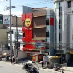 High-angle street view of the modern red, gray, and brown building facade of My Inn Calamba in Laguna, with passing tricycles and motorbikes.